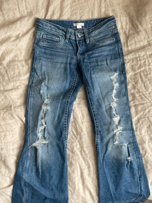 Blå slitna jeans från Gina Tricot - Säljer ett par blå jeans från Gina Tricot i storlek 152. Jeansen har slitningar och hål på båda benen för en trendig look. Klassisk femficksmodell med knapp och dragkedja. Perfekta för dig som gillar en avslappnad och cool stil. Skriv om ni har andra frågor!🥰