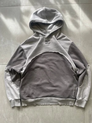 Grå patchwork hoodie från Bershka - Säljer en unik hoodie från Represent i två nyanser av grått med cool patchwork-design och råa sömmar. Hoodien har tryck på bröstet och nedtill, samt ribbade muddar vid ärmar och midja. Perfekt för dig som gillar streetwear och oversized look. Mått 📏 Längd från axel: 73cm Axelbredd: 53cm Skador 🔧: Litet hål på vänster armhåla, syns på bild  Storlek 🧍: L  Jag kan förhandla mig till lägre pris.🙋💵 Om du har några frågor, vänligen skriv till mig 🤗