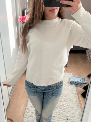 Vit stickad tröja med rund hals - Klassisk vit stickad tröja med rund halsringning och ribbade muddar vid ärmslut och nederkant. Tröjan har en rak passform och är perfekt för lager på lager. Enkel och stilren design som passar till det mesta.