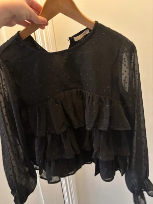 Svart volangblus med prickigt mönster - Säljer nu denna svarta glittriga blus i xxs, som jag köpt second han så den var för liten för mig, endast testad därav priset