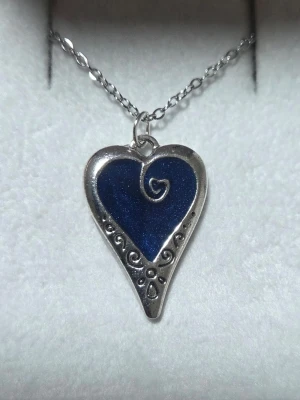Halsband med blått hjärthänge - Lyser  - Unikt halsband med ett hjärtformat hänge i silverfärg och blå emalj som lyser i mörkret efter att ha varit i dagsljus. Hänget har en swirl-design i mitten och dekorativa detaljer längs kanten. Kedjan är tunn och silverfärgad i rostfritt stål med förlängningskedja. Perfekt för dig som gillar smycken med lite extra wow-faktor. 🌸✍️🏻// Handgjord & skapad av mig, tillverkat med högkvalitativt självlysande pigment för ett tydligt sken och lång livslängd. Kedjan och hänget tål vatten och missfärgas inte.