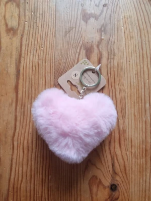 Rosa fluffigt hjärta nyckelring - Söt nyckelring med ett fluffigt hjärta i ljusrosa fuskpäls. Perfekt att hänga på väskan eller nyckelknippan för en gullig touch. Metallring och kedja i silverfärg.
