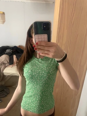Grön blommig ribbad topp - Säljer en grön ribbad topp med små vita blommor. Toppen har rund halsringning och korta ärmar. Materialet är stretchigt och sitter tight mot kroppen, perfekt för dig som gillar en slim fit look. Fråga järna om frågor💕❤️
