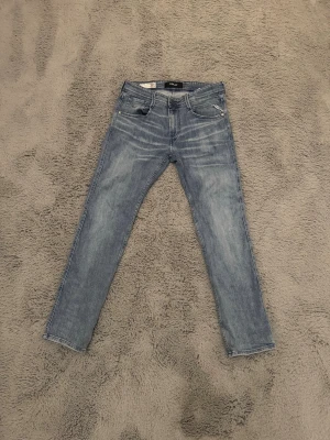 Ljusblå tapered jeans från replay - Säljer ett par ljusblå tapered jeans från replay med klassisk femficksdesign och snygga slitningar. Jeansen har normal midja, slim passform och är tillverkade i mjukt denimtyg. Perfekta för en avslappnad och trendig look.