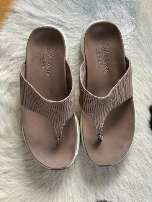 Beige Skechers Arch Fit sandaler storlek 38.5 i mycket fint sick  - Säljer ett par beige sandaler från Skechers med Arch Fit-sula i storlek 38.5.  De har breda, ribbade remmar i textil och tårem för extra komfort. Sulan är vit och ergonomiskt formad för bra stöd. Perfekta för dig som vill ha både stil och bekvämlighet. Mycket sparsamt använda!  Nypris 1300kr. 