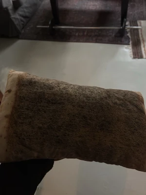 Rektangulär kudde med naturfärgat överdrag - Säljer en rektangulär kudde med naturfärgat tyg och ett brunt, lurvigt parti på ena sidan. Kudden har en mjuk och fluffig form och passar bra som dekoration eller stöd. Materialet ser ut att vara textil med ett inslag av naturfiber.