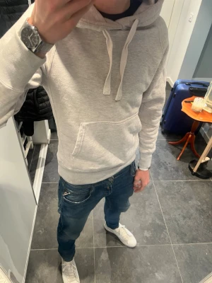 Russemerch hoodie grå  - Snygg ljusgrå hoodie med stor känguruficka framtill och justerbar huva med vita snören. Tillverkad i mjukt material som känns skönt mot huden. Perfekt för en avslappnad och stilren look.