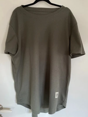 Ribbad t-shirt - En grön ribbad T-shirt i luftigt tyg med tryck på vänster nederkant