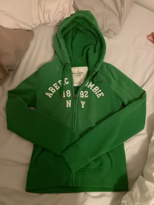 Abercrombie & Fitch grön hoodie - Snygg grön hoodie med dragkedja från Abercrombie & Fitch. Säljer den eftersom den aldrig har kommit till användning.
