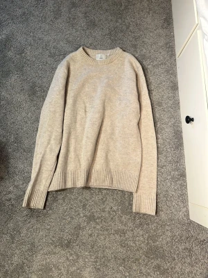 Beige stickad tröja - Snygg beige stickad tröja från Bläck i storlek M. Tröjan har rund halsringning och ribbstickade muddar vid ärmslut och nederkant. Perfekt för lager-på-lager och enkel att matcha med andra plagg. Nypris 800 kr