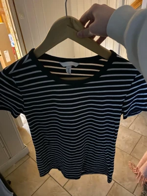 Svartvit randig t-shirt H&M - Säljer en svart t-shirt med vita horisontella ränder från H&M. T-shirten har rund halsringning och korta ärmar. Perfekt basplagg som är lätt att matcha till olika outfits.