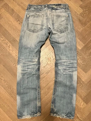 Ljusblå slitna jeans från G-Star - Säljer ett par ljusblå jeans från G-Star med slitningar och tvättade detaljer. Klassisk femficksmodell med raka ben och råa kanter vid bensluten. Snyggt mönstrad insida i midjan och tydliga sömmar på bakfickorna.