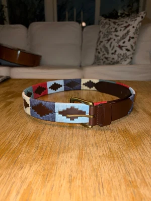 Multi-färgat bälte - Helt nytt och inplastat multi färgat broderat bälte i färgerna: mörkblå, ljusblå, vit, röd, grön. Extremt fräscht bälte som ger din outfit en sista detalj. Finns 5 olika storlekar att välja mellan: 80-110 cm. Men nu finns endast storlek 80 kvar! 