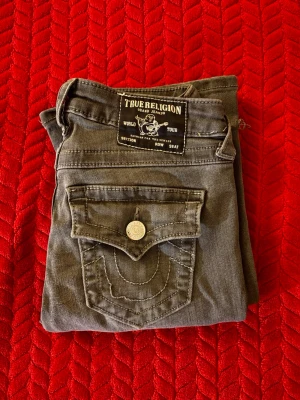 True Religion Becca grå bootcut jeans - Gråa True Religion Becca Mid Rise Bootcut jeans.            De blev lite för tight på midjan och har knappt använt dem. Jag är 168cm och längden på jeansen är rätt så bra, en av bakfickorna sömn är lite sönder men det syns inte så mycket.                                                                      Tack för ni kollar och ha en trevlig dag 💗💗