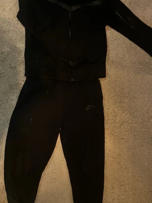 Svarta mjukisbyxor från Nike - Säljer ett par svarta mjukisbyxor från Nike med klassisk logga på benet. men på botten av byxorna är det rätt så slitet men går att fixa. Byxorna har dragsko i midjan och är tillverkade i ett mjukt och bekvämt material, perfekt för chill dagar. Matchar snyggt med en hoodie eller t-shirt.