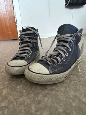 Converse Chuck Taylor All Star High - Klassiska Converse Chuck Taylor All Star high sneakers i marin blå canvas med vita gummisulor och tåhättor. Skorna har vita sko snören som har blivit lite missfärgade men går att tvätta bort , metallöljetter och den ikoniska loggan på sidan. Perfekta för en avslappnad och tidlös stil. Pris diskuteras 