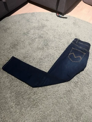 Mörkblå jeans från Morris - Snygga mörkblå jeans från Morris med klassisk femficksdesign och kontrastsömmar. Jeansen har smal passform och ikonisk broderad bakficka. Perfekta för en stilren och avslappnad look.