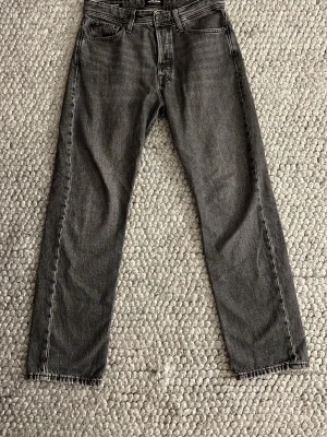 Grå relaxed jeans från Jack & Jones - Säljer ett par gråa relaxed fit jeans från Jack & Jones, modell Chris. Raka ben och hög midja. Jeansen är tillverkade i denim med en tvättad look och har bälteshällor samt knappgylf.