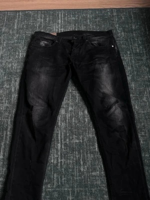 Svarta jeans från Dondup - Snygga svarta jeans från Dondup med diskret tvättad effekt på låren. Klassisk femficksmodell med knappgylf och raka ben. Jeansen är tillverkade i ett slitstarkt denimtyg som ger en cool och modern look.