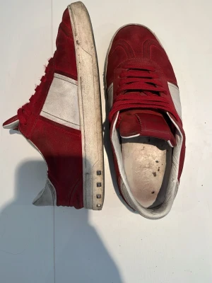 Röda sneakers från Valentino - Snygga röda sneakers från Valentino med vita detaljer på sidan och vit sula. Skorna har en klassisk låg siluett, röda skosnören och är tillverkade i mocka och läder. Perfekta för dig som vill sticka ut med stilrena och trendiga skor. Ingen box eller og medföljer. Obs priset är inte hugget i sten 