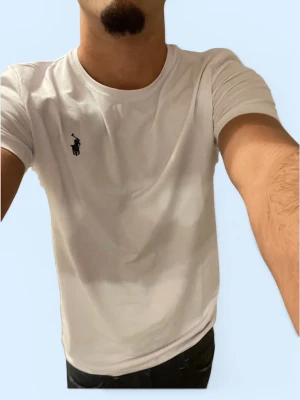 Vit t-shirt från Ralph Lauren - Klassisk vit t-shirt från Ralph Lauren med den ikoniska polospelaren broderad på bröstet. T-shirten har rund halsringning och korta ärmar. Tillverkad i mjuk bomull för en skön och avslappnad passform.