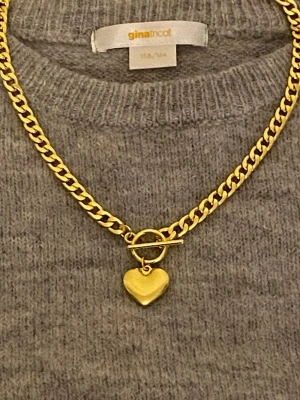 Guldfärgat halsband med hjärthänge - Stilrent halsband i guldfärgad rostfritt stålmed  kedja och ett hjärtformat hänge. Halsbandet har en snygg toggle-låsning framtill som ger en trendig touch. Perfekt accessoar för att lyfta din outfit.