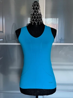 Blå linnetopp från Casall - Snygg blå linnetopp från Casall med v-ringad hals och figurnära passform. Tillverkad i ett stretchigt material som passar perfekt för träning eller en aktiv vardag. Ärmlös design och diskreta sömdetaljer för en sportig look.