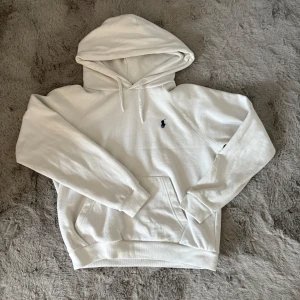 Vit hoodie från Ralph Lauren - Säljer en stilren vit hoodie från Ralph Lauren med det klassiska logotypbroderiet på bröstet. Tröjan har en känguruficka och justerbar huva. Perfekt för en avslappnad stil.                                                                               nypris 2195. 