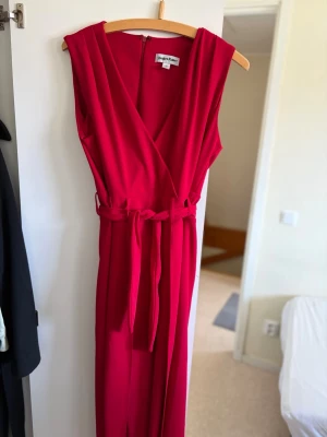 Röd ärmlös jumpsuit med knytskärp - Snygg röd ärmlös jumpsuit från Only & Sons med omlott-ringning och knytskärp i midjan. Vida ben och mjukt, följsamt tyg som ger en skön passform. Perfekt för dig som vill sticka ut med en färgstark look.