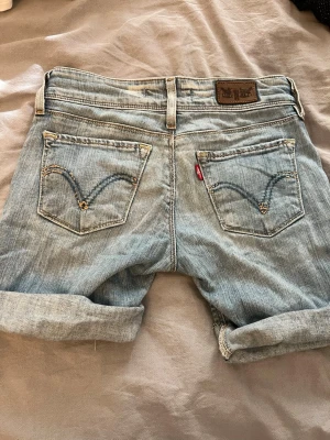 Levi's 571 ljusblå jeansshorts - Säljer ett par klassiska Levi's 571 lågmidjade jeansshorts i ljusblå denim. Modellen är slim fit med upprullade benslut och snygga bakfickor med broderad detalj. Perfekta för sommardagar och enkel att matcha med allt. De är avklippta jeans och väldigt små i storlek. De är storlek 26x32. Enligt mig sitter de typ som xxxs jeans eller mindre 
