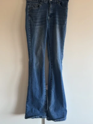 Blå bootcut jeans med detaljer low rise - Snygga blå bootcut jeans med klassisk femficksdesign och dekorativa sömmar samt nitar på bakfickorna. Jeansen har en lätt tvättad look och utsvängda ben. Perfekta för dig som gillar en retrostil och vill sticka ut lite extra.