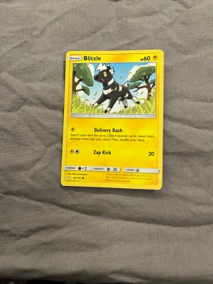 Pokémonkort Blitzle gul - Pokémonkort med motiv av Blitzle. Kortet är gult med illustration av Blitzle i en grönskande miljö. Text och symboler i svart och vitt, samt detaljer i orange. Kortet är av papp och har klassisk Pokémon-design.