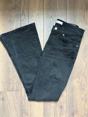 Svarta bootcut byxor Gina Tricot - Snygga svarta bootcut jeans från Gina Tricot med klassisk femficksdesign och silverfärgade nitar. Jeansen har utsvängda ben, perfekta för en trendig och avslappnad look. Tillverkade i stretchigt denim för extra komfort.