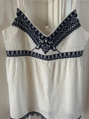 Vit linnetopp med blå broderi - Säljer en vit linnetopp med tunna axelband och mörkblå broderade detaljer. Jättefin och passar perfekt nu till sommaren!💙🐠