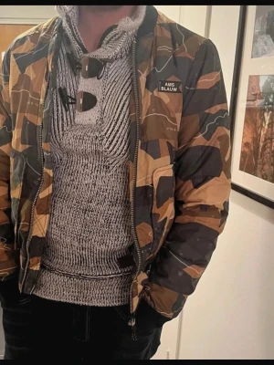 Scotch & Soda  - Säljer en snygg bomberjacka från Scotch & Soda med camouflagemönster i brunt, beige och svart. Jackan har dragkedja framtill, ribbade muddar och orange foder. Märket 'AMS BLAUW' syns på bröstet. Skriv till mig vid frågor eller pris! Inga defekter