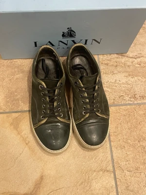 Lanvin svarta låga sneakers - Snygga svarta sneakers från Lanvin med lågt skaft och vita sulor. Skorna har klassisk snörning, metallfärgade öljetter och ovandel i läder och mocka. Perfekta för dig som gillar stilrena och exklusiva sneakers. Priset kan även diskuteras. Hör av er vid de minsta lilla