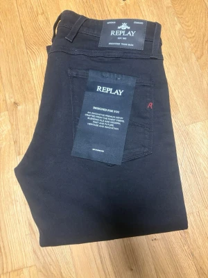 Svarta jeans från Replay - Snygga svarta jeans från Replay med klassisk femficksdesign och diskret röd detalj på bakfickan. Jeansen har en rak passform och är tillverkade i ett mjukt och stretchigt material som ger en skön känsla hela dagen.
