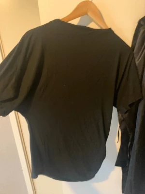 Svart basic t-shirt - En enkel svart t-shirt med korta ärmar och rund hals. Perfekt till jeans eller shorts och funkar året runt. T-shirten är i mjukt material och har en klassisk passform. Med en scrunch vid sidan