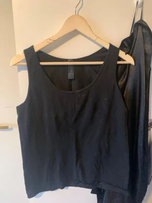 Svart linnetopp från H&M - En basic svart linnetopp från H&M med rund halsringning och ärmlös design. Perfekt att styla lager på lager eller bära som den är. Tillverkad i mjuk bomull som känns skön mot huden.