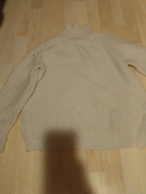 Beige stickad polotröja - Mysig beige stickad polotröja med lång ärm och grovstickad struktur. Tröjan har hög krage och avslappnad passform, perfekt för kyliga dagar. Passar dig som gillar enkel och klassisk stil.