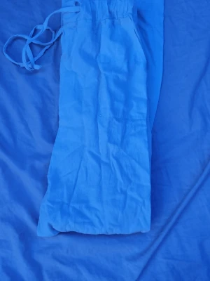 Ljusblåa linnebyxor med dragsko - Säljer ett par ljusblåa linnebyxor med avslappnad passform och elastisk midja med dragsko. Byxorna har raka ben och är tillverkade i ett svalt linnematerial, perfekta för varma dagar. Enkla att matcha och superbekväma.