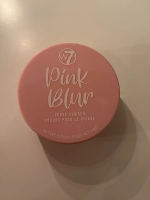 W7 Pink Blur Loose Powder - Använd 1 gång så är typ helt full! W7 Pink Blur Loose Powder är ett ansiktspuder i en rund, rosa burk. Pudret är veganskt och PETA-godkänt, perfekt för att fixera foundation och ge en mjuk, suddad finish. Innehåller bland annat majsstärkelse och aluminiumstärkelse. Vikt: 20g.