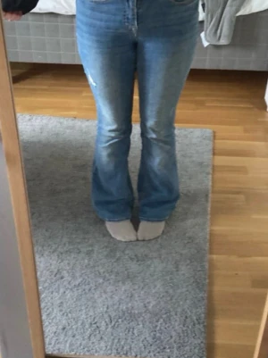 Ljusblå bootcut jeans - Säljer ett par ljusblå bootcut jeans med klassisk femficksdesign och normalhög midja. Jeansen har lätt utsvängda ben och är tillverkade i ett stretchigt denimtyg som sitter snyggt. Perfekta för en avslappnad och trendig look. 