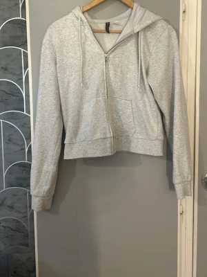 Ljusgrå hoodie från H&M Divided - Ljusgrå hoodie med dragkedja från H&M Divided. Modellen har huva med dragsko, två fickor framtill och ribbade muddar vid ärmslut och nederkant. Mjuk insida i bomullsblandning, perfekt för en avslappnad stil. Storlek m men skulle säga att de passar xs- s