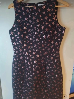 Svart kortklänning med stjärnmönster - Supersnygg svart kortklänning från Warehouse med metallicfärgade stjärnor över hela klänningen. Ärmlös modell med rund hals och figurnära passform. Materialet är polyester med glittrig finish som verkligen sticker ut.