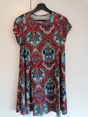 Röd mönstrad klänning från Nelly - Röd kortärmad klänning i orientaliskt mönster köpt på Nelly.com. Rund halsringning och avslappnad passform. Kan med fördel användas med ett fint skärp. 