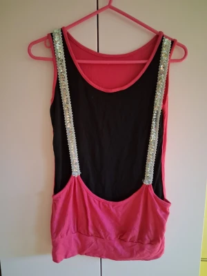 Svart och rosa linnetopp med paljetter - Cool linnetopp i svart och rosa med breda axelband täckta av silvriga paljetter. Toppen har en lös passform och djup urringning, perfekt för en trendig och avslappnad stil.