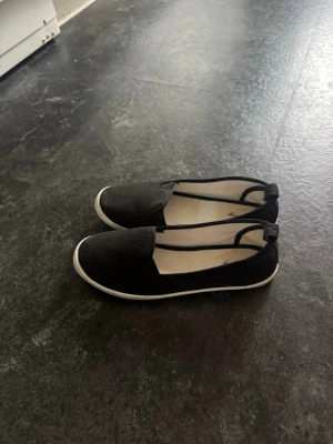 Svarta ballerinaskor från Alley - Snygga svarta ballerinaskor från Alley med vit sula och enkel slip-on design. Skorna har rund tå och är tillverkade i textilmaterial med mjuk innersula för extra komfort. Perfekta för en avslappnad och stilren look. Storlek 36