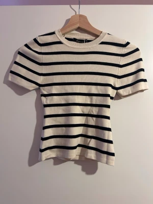 Randig stickad topp från Ginatricot - Randig stickad topp från Ginatricot i vit och svart. Modellen har korta ärmar, rund halsringning och en slim passform. Materialet är mjukt och ribbat, perfekt för att skapa en clean och stilren look.