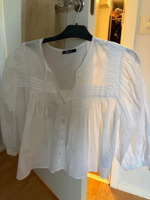 Vit blus med puffärm från Gina Tricot - Snygg vit blus från Gina Tricot med knappar framtill och dekorativa veck vid axlar och bröst. Blusen har puffiga långärmar och en lös, luftig passform. Perfekt för en trendig och stilren look. Nypris för tröjan är 399!